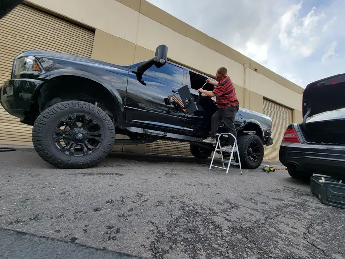 Alex on a step stool repairing a black pickup truck outside